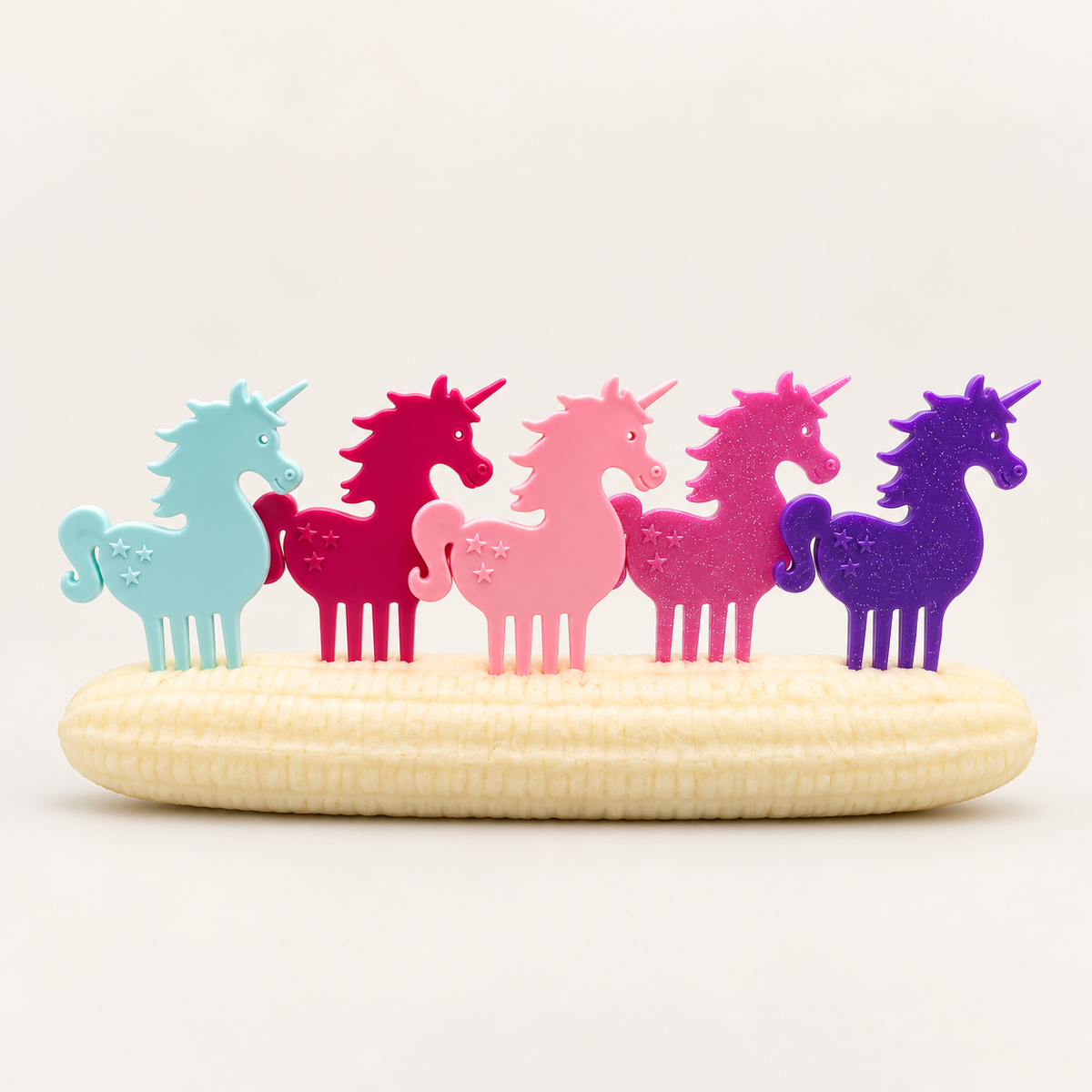 Fünf Einhorn-Snackpiekser in Mint, Pink, Rosa, Glitzerpink und Glitzerlila, in eine geschälte Banane gesteckt.
