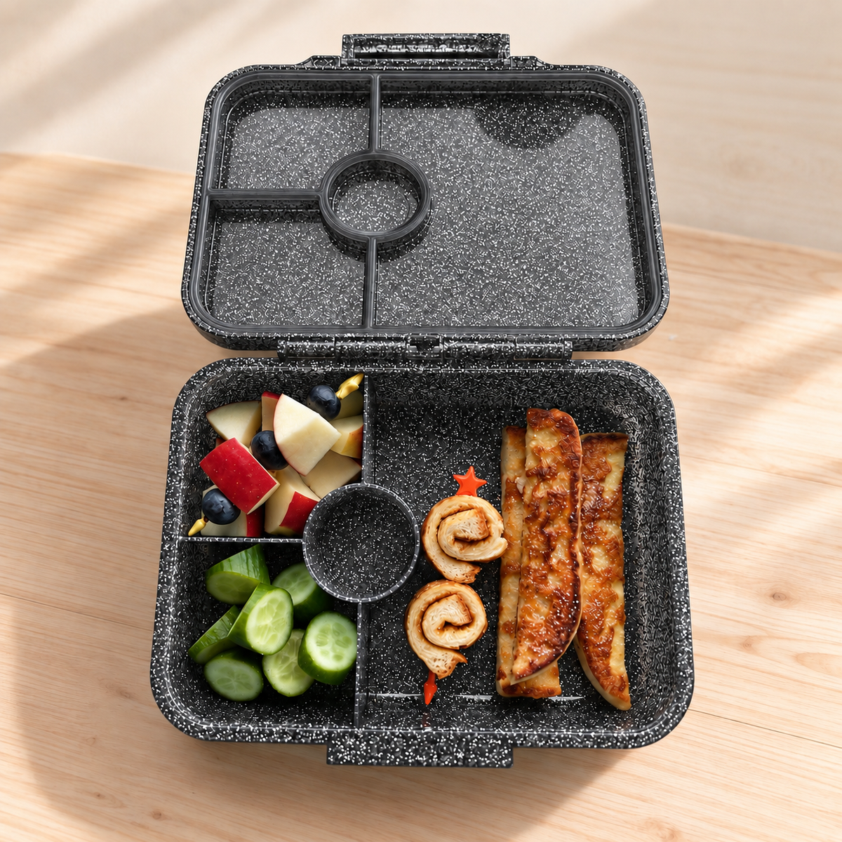 Geöffnete LEKKABOX Glamour Glitzer-Brotdose in Black mit vier Fächern, gefüllt mit Obst, Gurken und Gebäck.